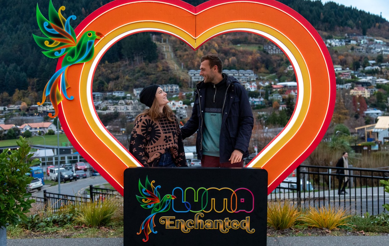 Couple taking a photo in front of illuminated love heart billboard