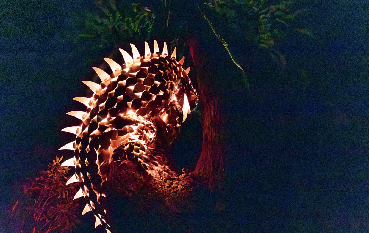 Glowing tuatara sculpture climbing a tree